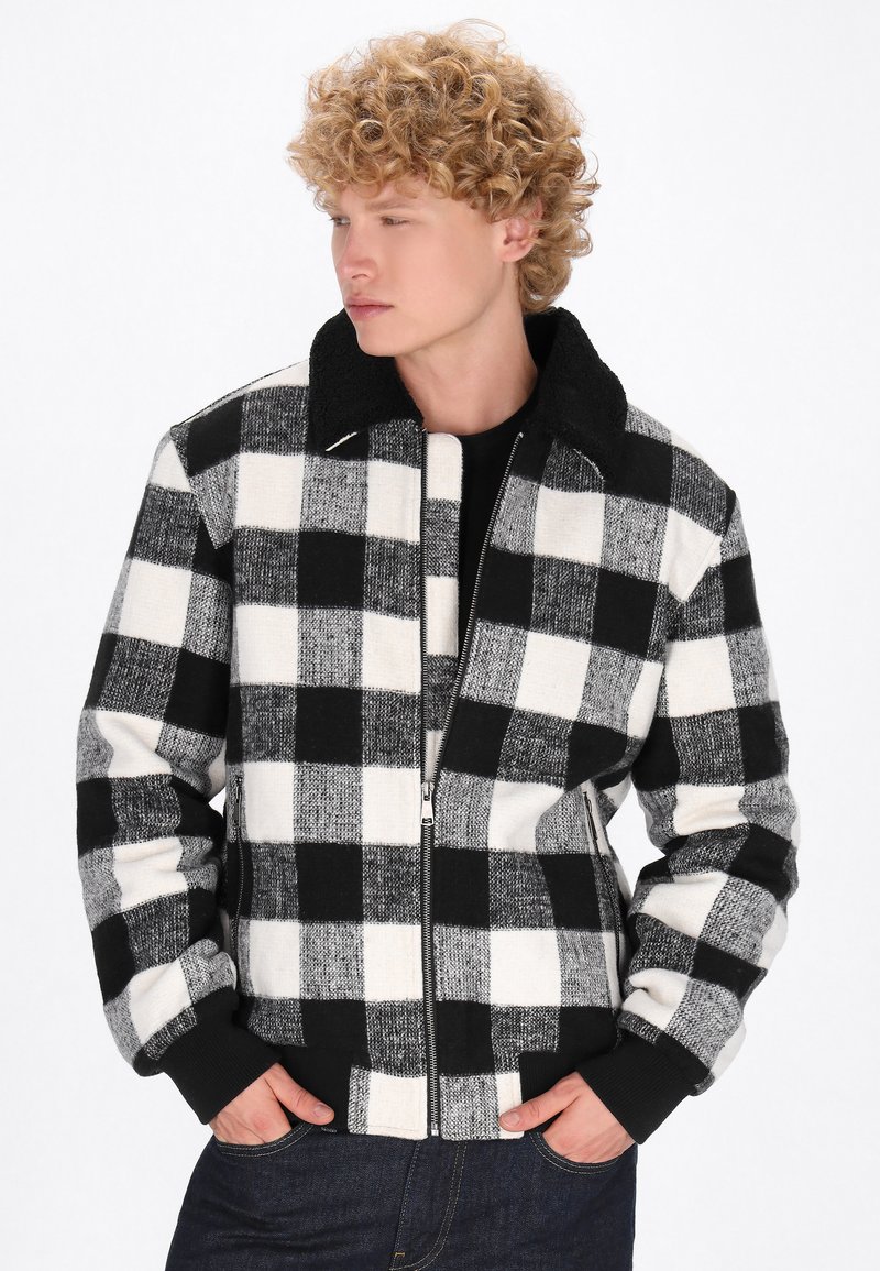 Sort-hvid ternet jakke med lynlås foran, struktureret materiale og sort krave. Har ribbede manchetter og kant.