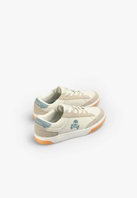 Beige Sneaker mit einem strukturierten Obermaterial, hellblauen Akzenten, einem Skull-Logo und einer orangefarbenen Gummisohle. Sie haben weiße Schnürsenkel und einen gepolsterten Schaft.