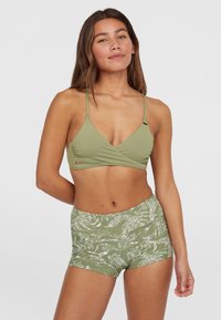 Grüner Bikini-Oberteil mit verstellbaren Trägern und Wickeldesign, kombiniert mit grünen Shorts mit einem weißen abstrakten Muster. Glatte Textur.