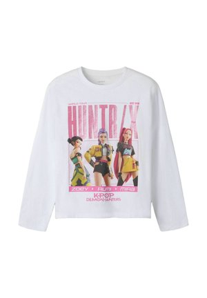 Chemise blanche à manches longues avec trois personnages féminins animés en tenues colorées et texte rose indiquant "HUNTR/X KPOP Demon Hunters."