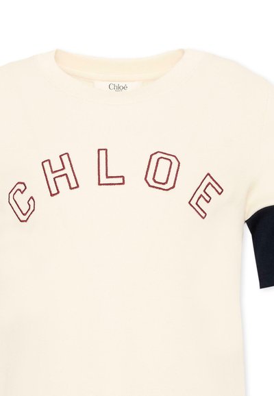 Maglietta a maniche corte color crema con manica nera e lettere rosse contornate che formano la parola CHLOE sul petto.