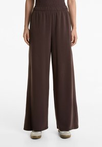 Braune, weit geschnittene Hose aus weichem Stoff mit elastischem Bund. Glatte Textur ohne sichtbare Muster oder Hardware.