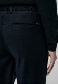 Zwarte, op maat gemaakte broek met een elastische tailleband, een gladde textuur en een onopvallende achterzak met minimale hardware-details.