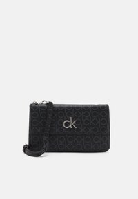 Černá crossbody taška s opakujícím se vzorem "CK", stříbrnými detaily, zipovým uzávěrem a nastavitelným popruhem pro všestranné nošení.