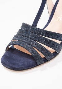 Sandale bleu marine à bout ouvert avec quatre brides croisées scintillantes et une semelle en daim.