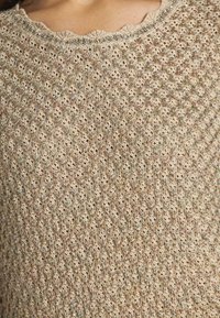 Maglione lavorato a maglia con scollatura a scallop, caratterizzato da un colore beige chiaro e un motivo testurizzato con sottili fili metallici e paillettes sparse.