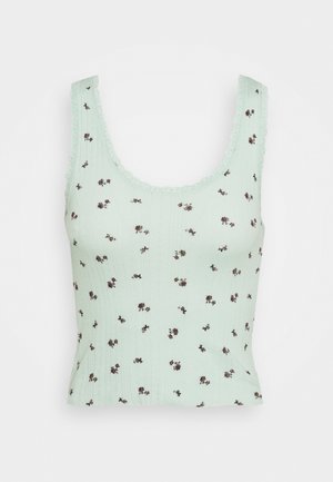 Haut court sans manches vert clair avec de petits imprimés floraux foncés et des bords festonnés sur les bretelles et l'encolure.