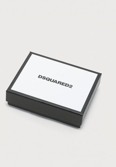 Boîte rectangulaire en noir et blanc avec le logo DSQUARED2 centré sur le couvercle blanc, posée sur une surface grise claire unie.
