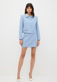 Completo in tweed di un blu chiaro, composto da un giacca corta con colletto, chiusura a bottoni e dettagli sulle tasche, abbinato a una mini gonna coordinata.