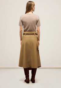 Jupe marron taille haute avec un large ourlet, ornée d'une ceinture contrastante sombre. Portée avec un haut ajusté à manches courtes de couleur marron clair et des bottes jusqu'au genou.