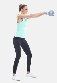 Lyseblå turkis tank top, sorte leggings og hvide sneakers; udfører en kettlebell-øvelse med en grå kettlebell.