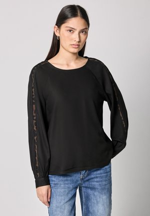 Black blouse with long sleeves featuring a raglan design and sheer leopard print accents along the sleeves. Smooth fabric, relaxed fit.
