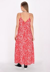 Rochie maxi roșie cu un model abstract alb, spate în formă de V, bretele subțiri și o croială lejeră, purtată cu adidași negri.