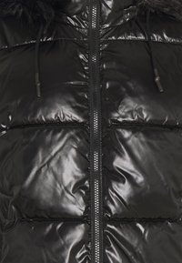 Svart puffjacka med glänsande yta, som har en dragkedja längs hela framsidan, justerbara snoddar i huvan och horisontella quiltade sektioner.