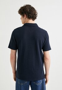 Mörkblå kortärmad polo med ribbad textur och klassisk krage. Baksidan har en ren design utan synliga logotyper eller mönster.