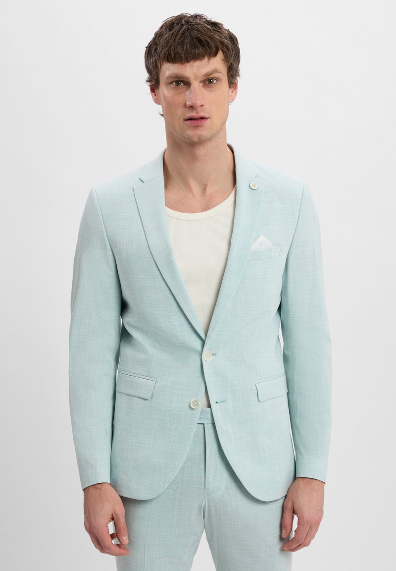 Helles blaues, strukturiertes Anzug mit Reverskragen, zwei Knöpfen und aufgesetzten Taschen. Kombiniert mit einem weißen gerippten Hemd. Lässiges, aber maßgeschneidertes Design.