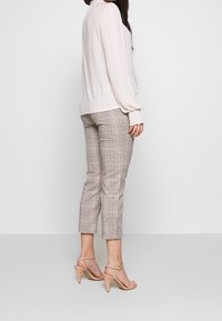 Ljusrosa ribbad tröja med medellånga ärmar, tillsammans med figurnära, rutiga byxor i beige och brunt. Beige högklackade sandaler fulländar looken.