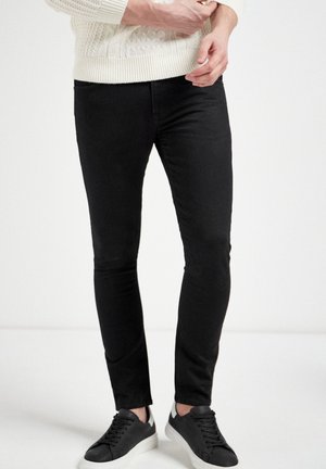 Jeans skinnys negros con una textura suave, con una cintura de altura media. Combinados con zapatillas negras y un suéter de punto color crema.