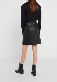 Mustasta nahasta valmistettu A-linjainen hame, jossa on sileä pinta ja keskellä takana sauma, yhdistetty kapeisiin mustiin nilkkureihin.