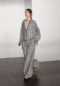 Gråt ternet sæt til afslapning med en løstsiddende skjorte med knapper og dyb V-hals samt bukser med vide ben og lommer. Glat tekstur.