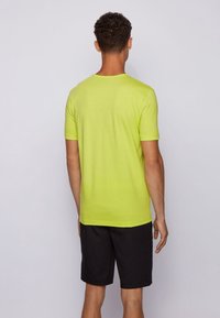 Neon green short-sleeved T-shirt with a round neckline, paired with black shorts. Smooth texture, simple design, no visible patterns or logos.