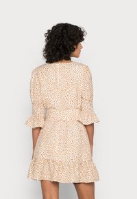 Vestido de cor creme com estampa floral, mangas curtas e evasê, e barra com babados. Apresenta uma cintura ajustada e um decote redondo.