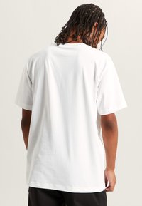 Bílý bavlněný tričko s krátkým rukávem, volný střih a zadní pohled. Hladký povrch, žádné viditelné vzory nebo grafika.