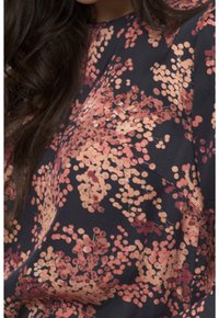 Haut à imprimé floral avec un fond bleu marine parsemé de pois pêche et bordeaux. Manches courtes, encolure ronde et texture de tissu douce.