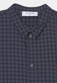 Marineblau kariertes Hemd aus weichem Stoff, mit spitzem Kragen, Knopfverschluss und einer Brusttasche mit subtiler Textur.