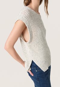 Top senza maniche di colore chiaro, con texture e design a costine, fianchi aperti e orlo spaccato, abbinato a jeans blu scuro.