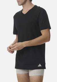 Black v-neck t-shirt made of cotton blend fabric. Short sleeves, relaxed fit, and Adidas logo on the lower right side.