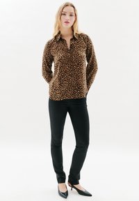 Camicia a righe leopardate, con bottoni, in tessuto marrone e nero, abbinata a pantaloni neri slim e tacchi a punta neri. Texture liscia.