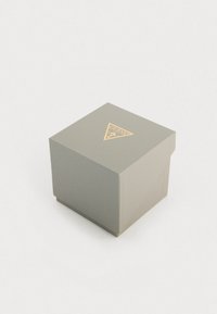 Scatola di imballaggio quadrata grigia con superficie texturizzata, caratterizzata da un logo triangolare dorato sulla parte superiore. Stile di chiusura indicato da un leggero intaglio.