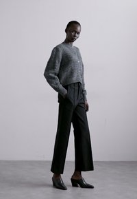 Gray knitted cardigan with a textured pattern, paired with tailored black wide-leg pants and dark heeled mules. Simple, modern design.