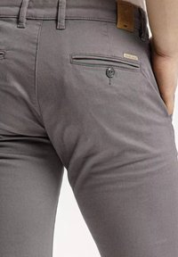 Szare legginsy o wąskiem kroju, z guzikiem w tylnej kieszeni oraz delikatną fakturą. Widoczne są szlufki na pasek i metka z logo.