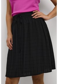 Jupe noire, longueur genou, avec une taille élastique et un cordon de serrage ajustable. Présente des rayures texturées subtiles sur l'ensemble du tissu.