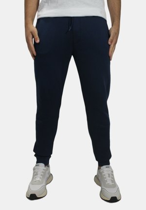 Joggers blu navy realizzati in tessuto morbido, con vita regolabile, gambe affusolate e tasche laterali. Abbinati a sneaker bianche.