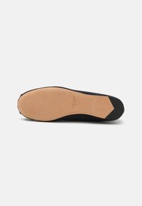 Shoe preto de salto baixo com um cabedal de tecido liso. A sola é de couro bege com um acabamento texturizado e uma ligeira forma pontiaguda na ponta.