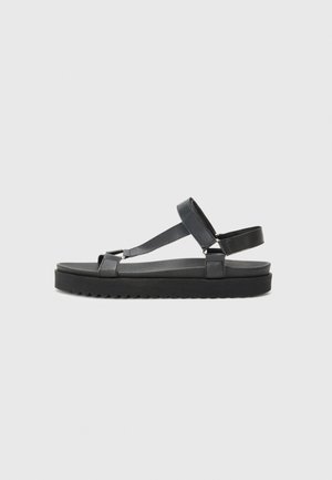 Sandali neri con cinturini, suola piatta, realizzati in materiale sintetico. Presentano un design semplice con una soletta strutturata e cinturini regolabili.