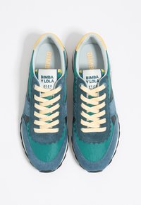 Turkusowe i niebieskie tenisówki z materiałów zamszowych i tkaninowych, z falistymi detalami, żółtymi sznurowadłami i czarnymi gumowymi podeszwami. Widoczna metka marki.
