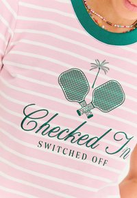 Różowo-biała koszula w paski z zielonym kołnierzykiem, grafika skrzyżowanych wioseł i palmy oraz napis "Sprawdzono Wyłączono".