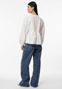 Blouse en coton blanc avec des manches bouffantes, dos dégagé et détail froncé à la taille, associée à un jean en denim foncé, ample.