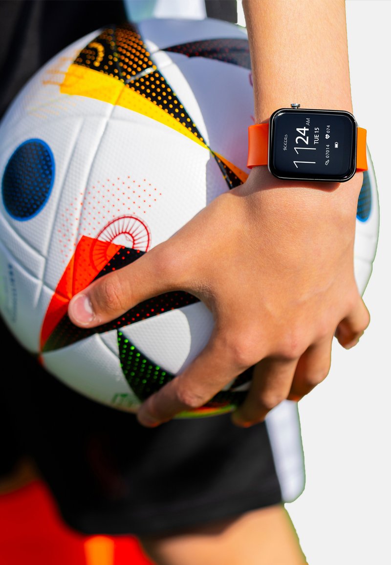 Un ballon de football blanc avec des motifs colorés est tenu par une main portant une montre connectée noire avec un bracelet orange, affichant l'heure.