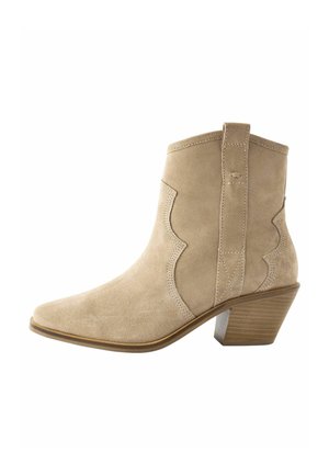 Bottine beige en daim avec coutures festonnées, languette, bout pointu et talon bloc empilé.