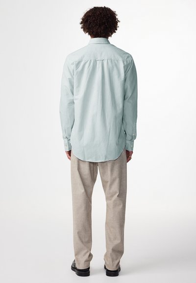 Camicia a righe blu chiaro con bottoni e maniche lunghe, piega sul retro e orlo arrotondato, abbinata a pantaloni beige chiaro e scarpe scure.