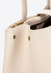 Borsa a spalla in pelle beige con hardware dorato, dotata di due manici e chiusura con zip. Texture liscia con cuciture minime e dettagli in metallo.