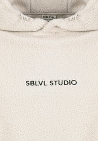 Weißer Fleece-Pullover mit hohem Kragen und Reißverschluss. Auf der Vorderseite befindet sich schwarzer Text "SBLVL STUDIO". Weiche, strukturierte Oberfläche.