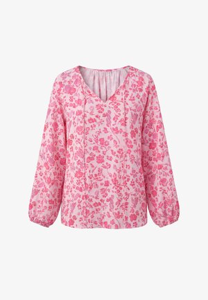 Roze blouse met lange mouwen, V-hals en bloemenpatroon in donkerdere roze tinten op een lichtroze achtergrond.