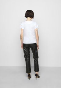 Camiseta blanca de manga corta combinada con pantalones de cuero negros y zapatos de tacón alto negros, vista desde atrás, mostrando un estilo minimalista.