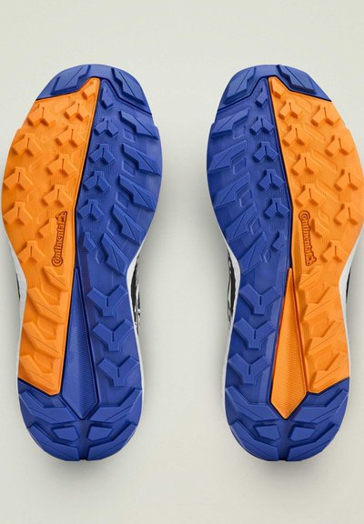 Trailové bežecké topánky s čierno-bielym zvrškom, modro-oranžovou gumovou podrážkou a textúrovanými gripovými vzormi, s logom Continental.